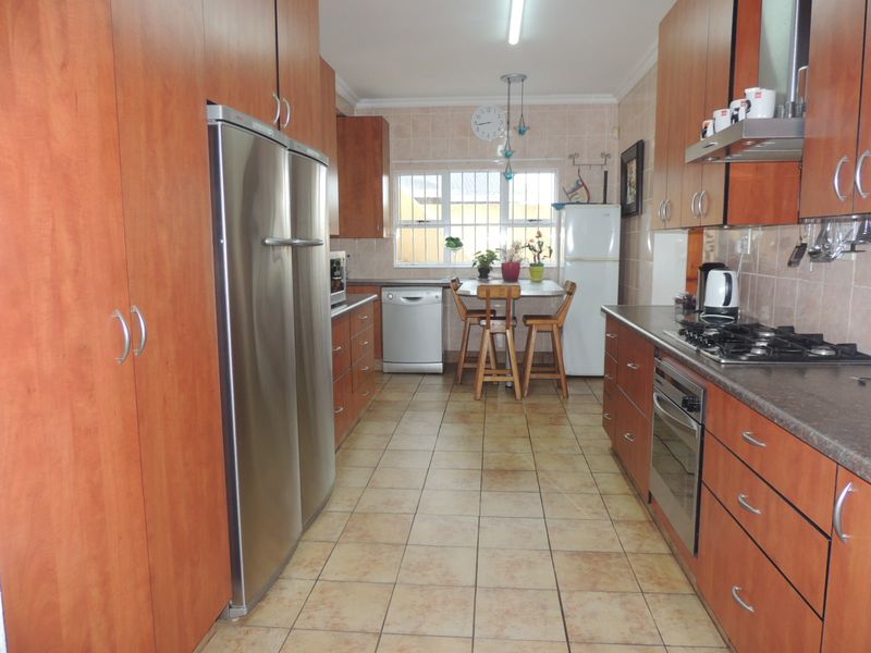 A functional kitchen featuring wood-finish cabinetry, tiled flooring, a gas hob, built-in oven, and a breakfast nook area by the window.