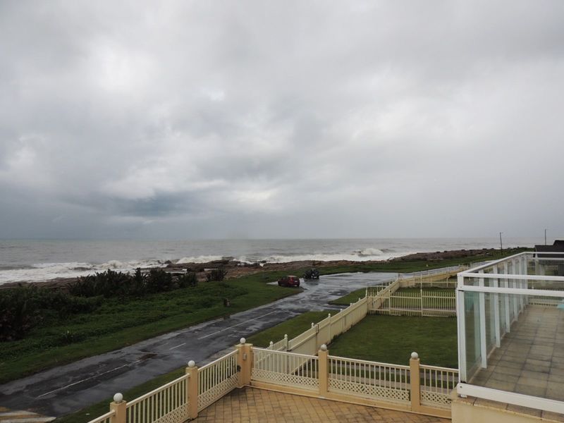 Elevated coastal view overlooking the ocean, featuring a paved terrace with a glass balustrade and surrounding perimeter fencing.