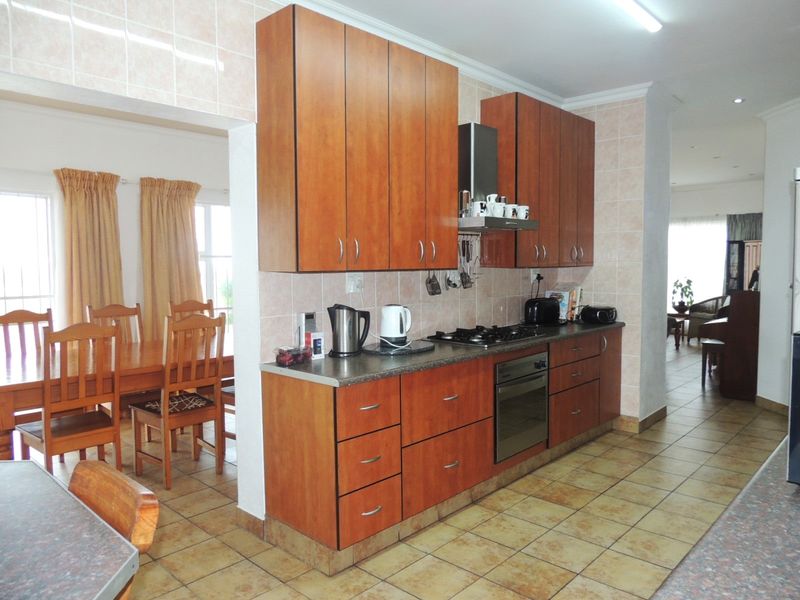 Functional kitchen featuring wood-finish cabinetry, built-in oven and gas hob, tiled splashbacks, and durable floor tiles, seamlessly connected to the dining area.