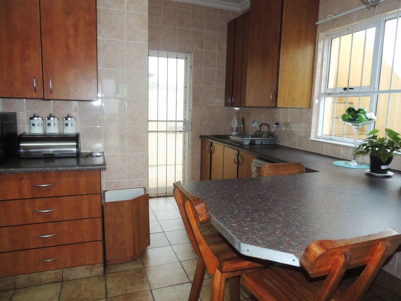 A functional kitchen featuring wood-look cabinetry, tiled surfaces, and a built-in breakfast nook, with direct access to an exterior security door.