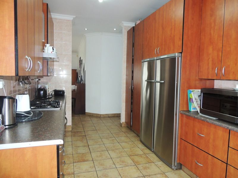 A functional kitchen featuring wood-finish cabinetry, tiled flooring, a gas hob, and integrated stainless steel appliances.