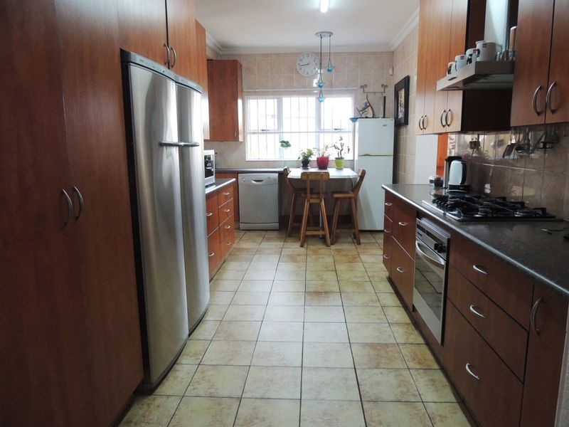 A functional kitchen featuring wood-finish cabinetry, tiled flooring, a gas hob, and built-in oven, offering a practical layout with ample storage space.