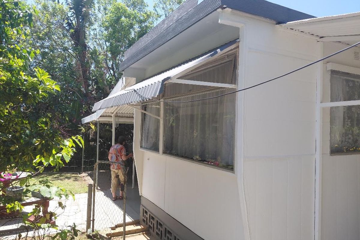 Rear exterior view of the property showing the building facade, corrugated metal roofing, and surrounding garden area.