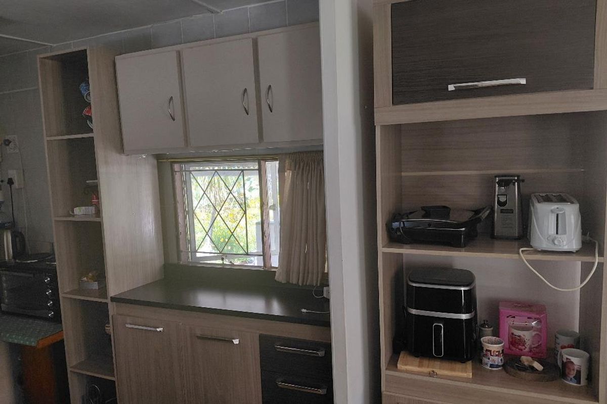 A functional kitchen area featuring built-in cabinetry, laminate countertops, and a window with a security gate.