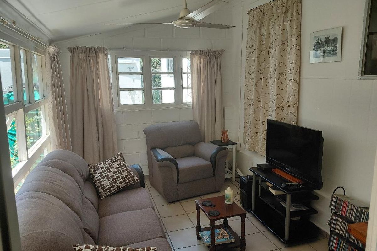 A cozy living room featuring tiled flooring, cinder block walls, and a ceiling fan, with ample natural light from multi-pane windows.