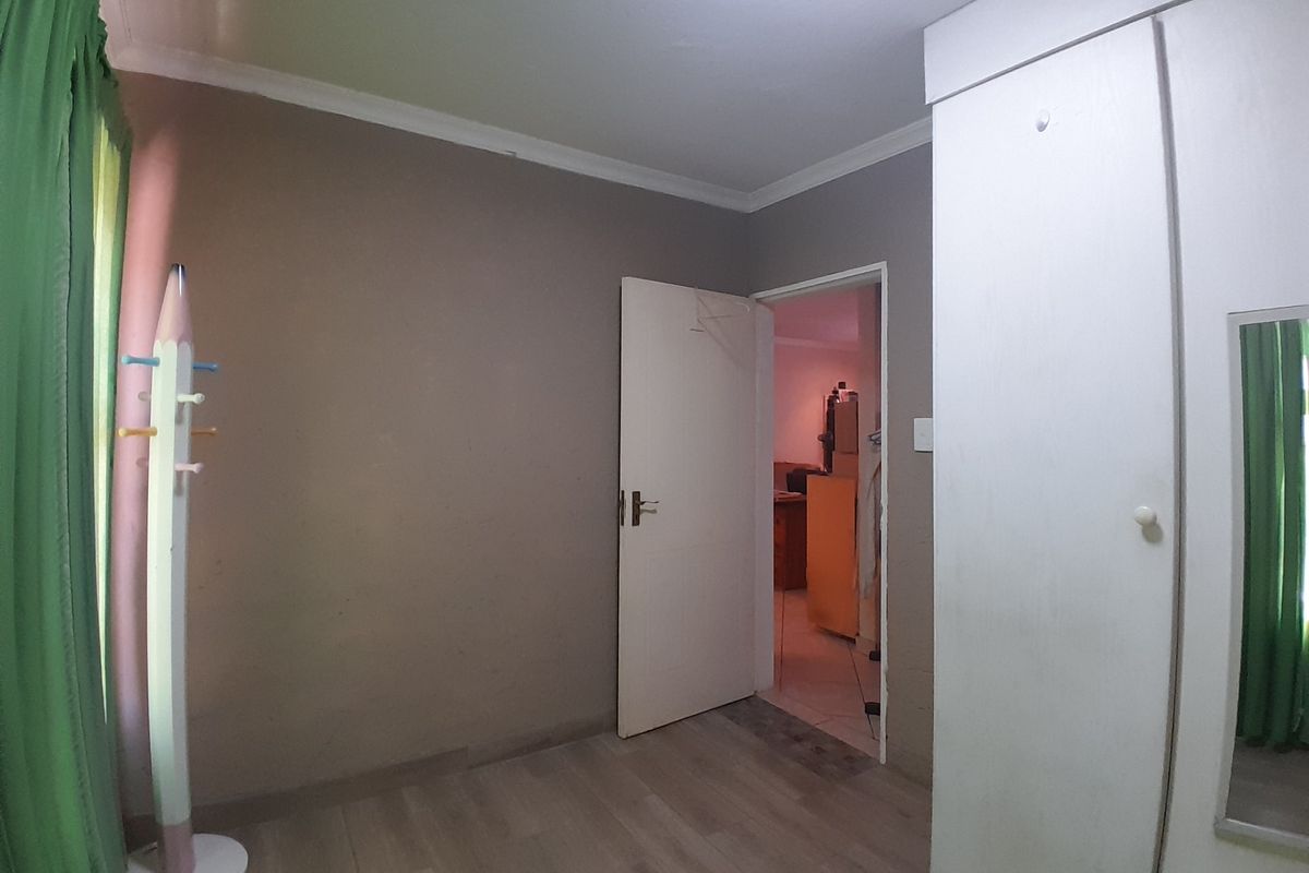 A bedroom featuring laminate flooring, built-in wardrobe storage, and neutral wall finishes, offering a functional space ready for personalization.