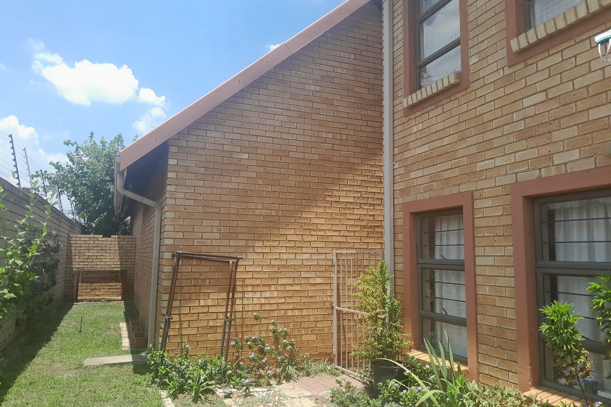 A side view of the property featuring face brick exterior walls, aluminium window frames with security bars, and a small garden area.