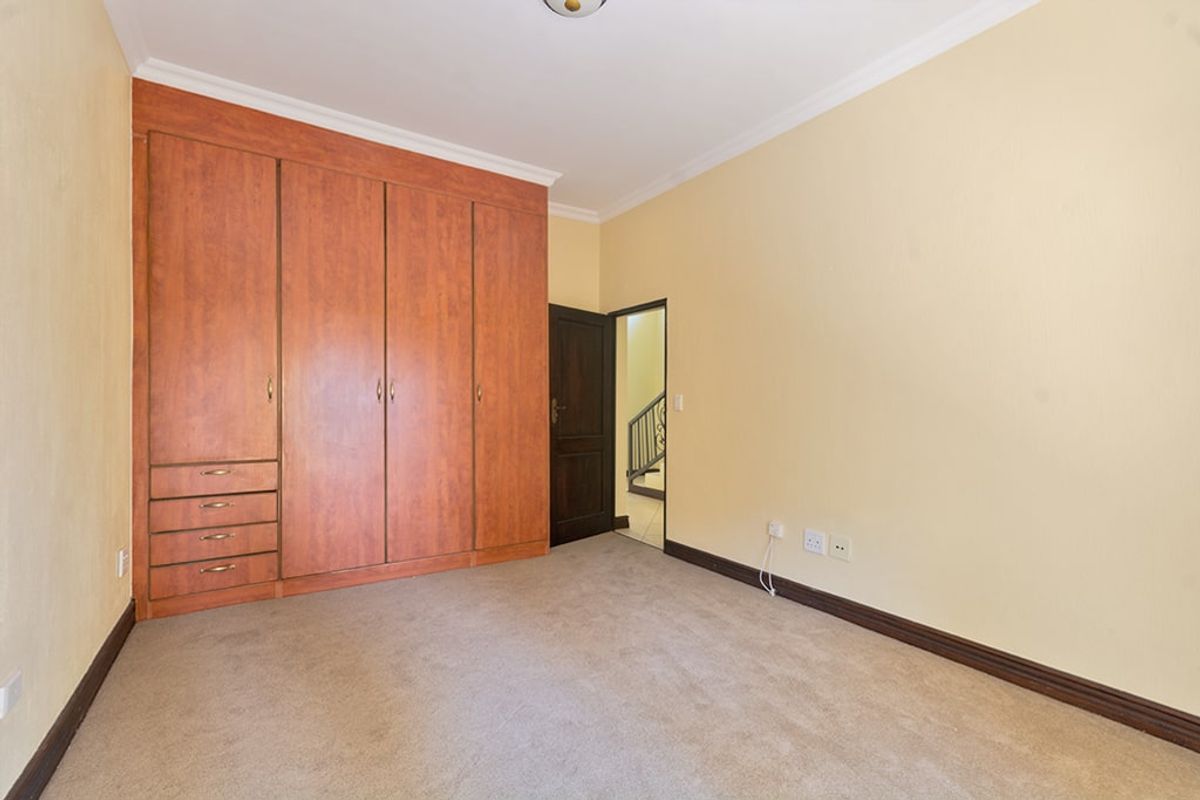 A spacious, empty bedroom featuring neutral walls, carpeted flooring, and extensive built-in wooden cupboards for storage.