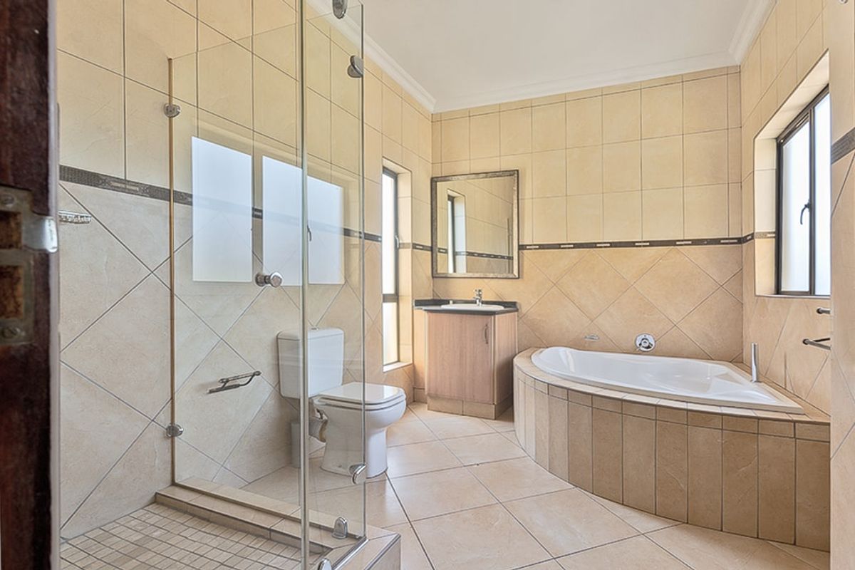 A spacious bathroom featuring a corner bathtub, a glass-enclosed shower, a vanity unit with a basin, and neutral ceramic tiling throughout.