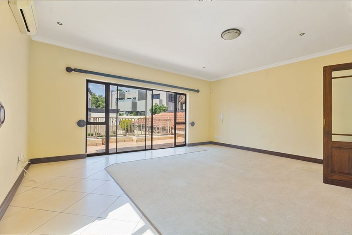 Spacious living room featuring a mix of tiled and carpeted flooring, split-system air conditioning, and large sliding glass doors opening to an outdoor balcony.