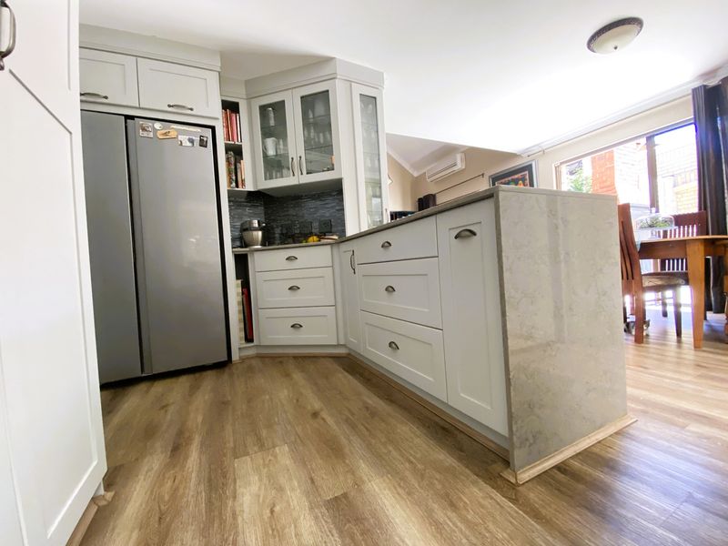Modern kitchen featuring light grey shaker-style cabinetry, a stone-look island bench, and durable laminate flooring, seamlessly integrated into an open-plan living space.