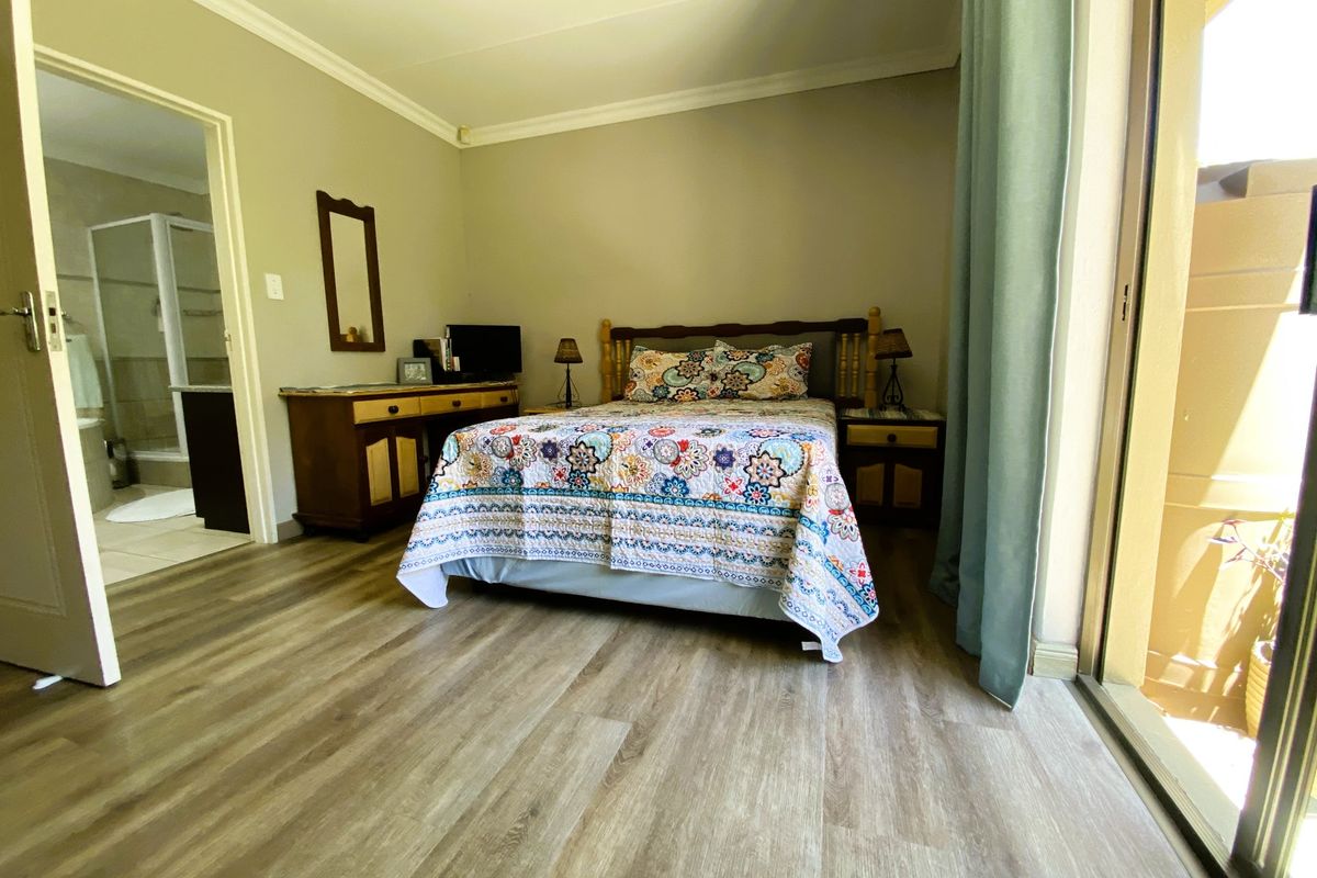 A well-lit bedroom featuring modern laminate flooring, cove cornicing, and direct access to an en-suite bathroom and a private balcony through sliding glass doors.