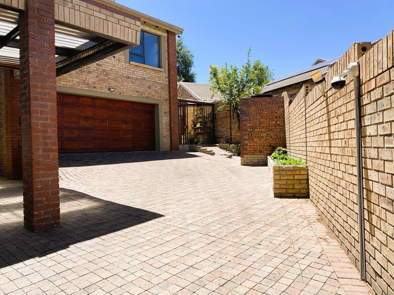 A well-maintained paved driveway leading to a double garage, featuring brick boundary walls, a built-in planter box, and a covered carport area.