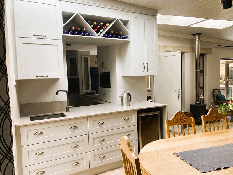 A well-appointed kitchen area featuring custom white cabinetry, stone countertops, integrated wine storage, and a cozy wood-burning stove in the adjacent living space.
