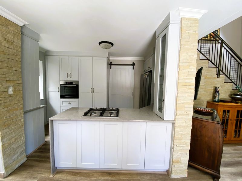 Modern kitchen featuring light grey cabinetry, stone countertops, a built-in gas hob, and a decorative stone veneer feature wall.