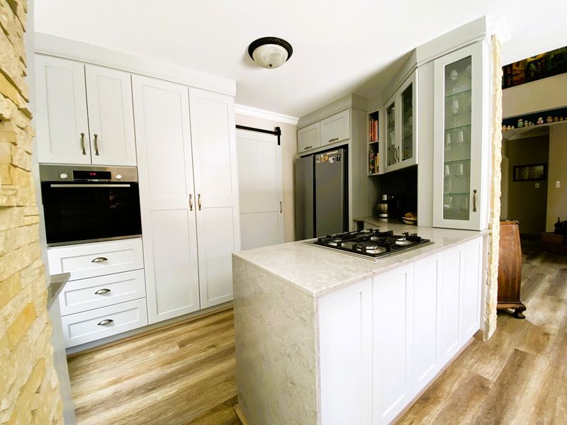 Modern kitchen featuring white shaker-style cabinetry, stone countertops, built-in oven, gas cooktop, and elegant glass-front display cabinets with wood-look flooring.