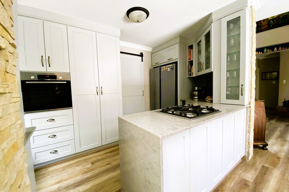 Modern kitchen featuring white shaker-style cabinetry, stone countertops, built-in oven, gas cooktop, and elegant glass-front display cabinets with wood-look flooring.