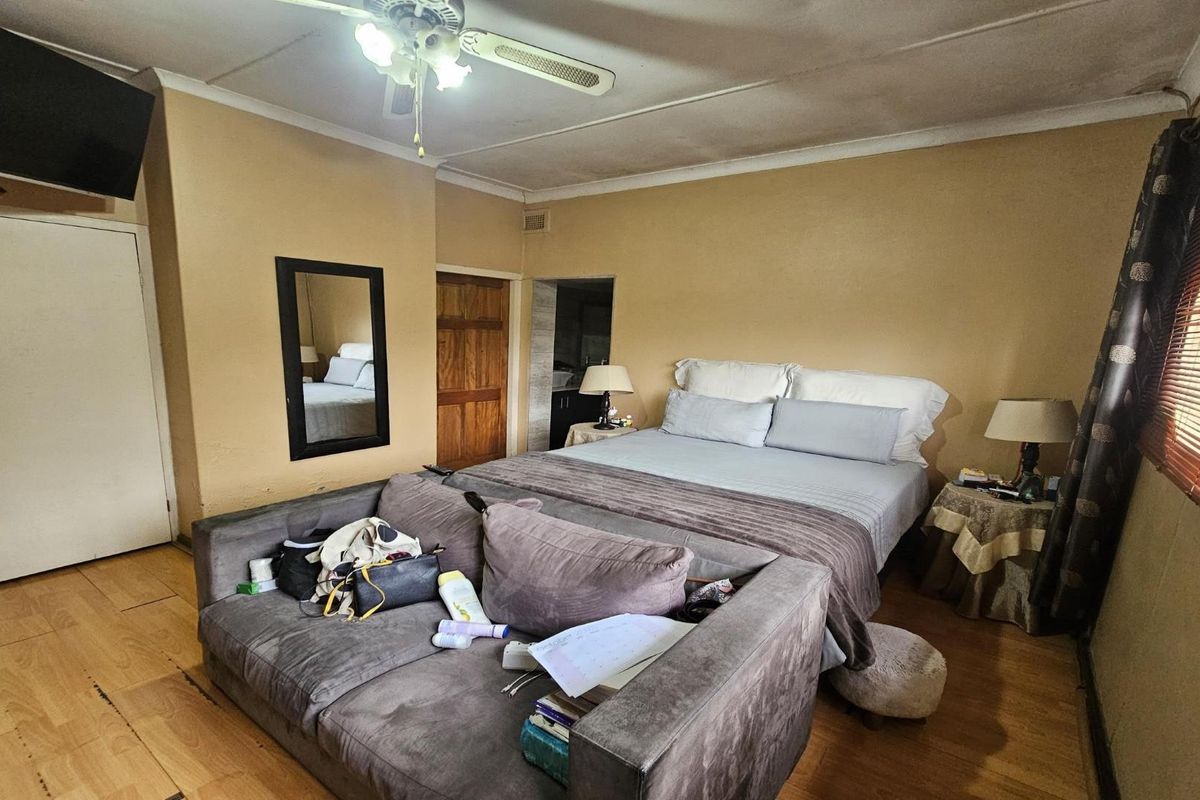 A bedroom featuring laminate flooring, a ceiling fan, and neutral wall tones, offering a functional space with potential for cosmetic updates.