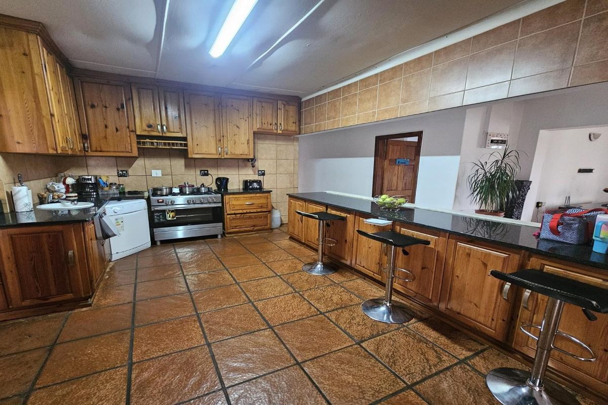 Spacious kitchen featuring extensive wooden cabinetry, granite countertops, a breakfast bar, and a freestanding gas stove with tiled flooring throughout.