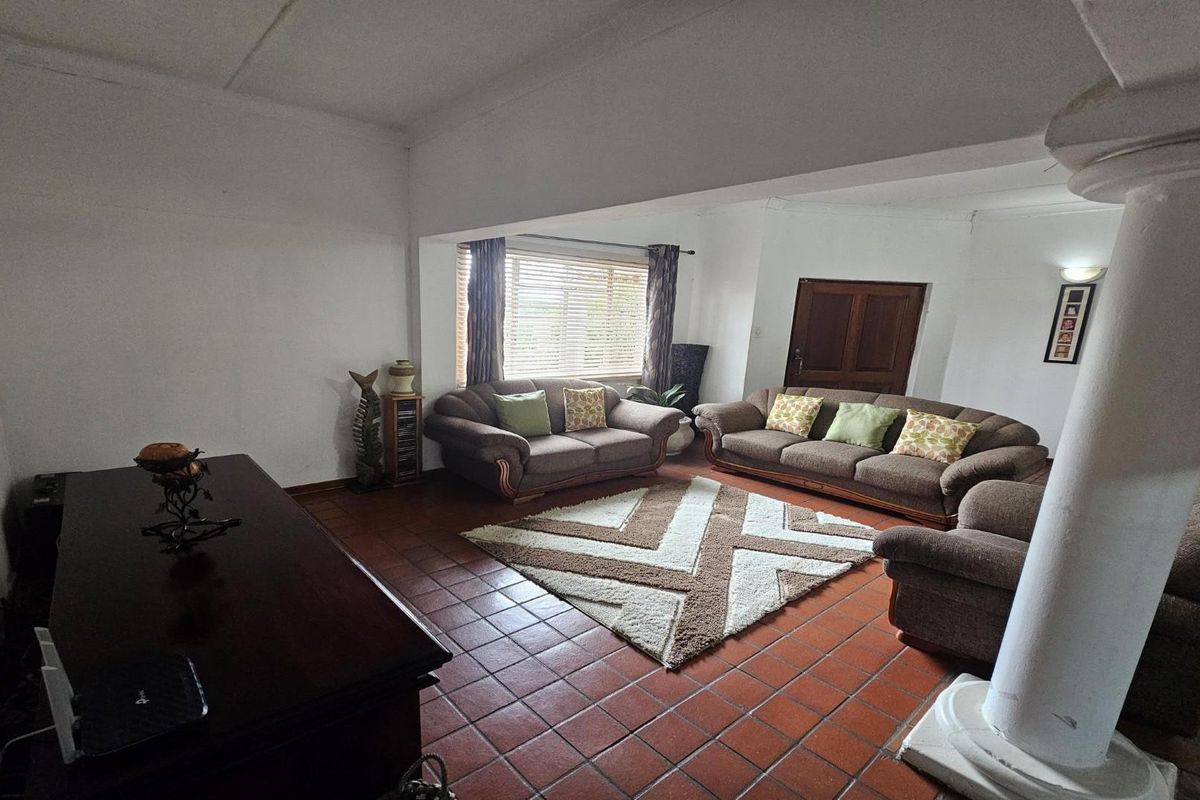 Spacious living room featuring terracotta floor tiles, a decorative structural column, and natural light through venetian blinds.