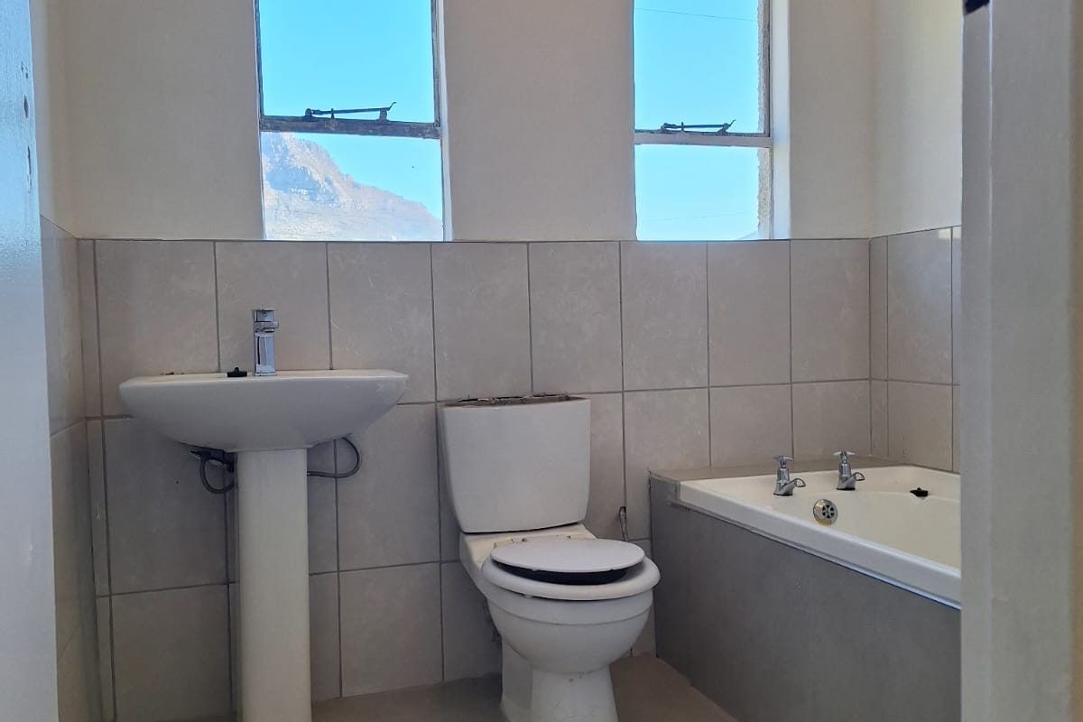 A functional bathroom featuring a pedestal basin, standard toilet, and a built-in bathtub with neutral wall and floor tiling.