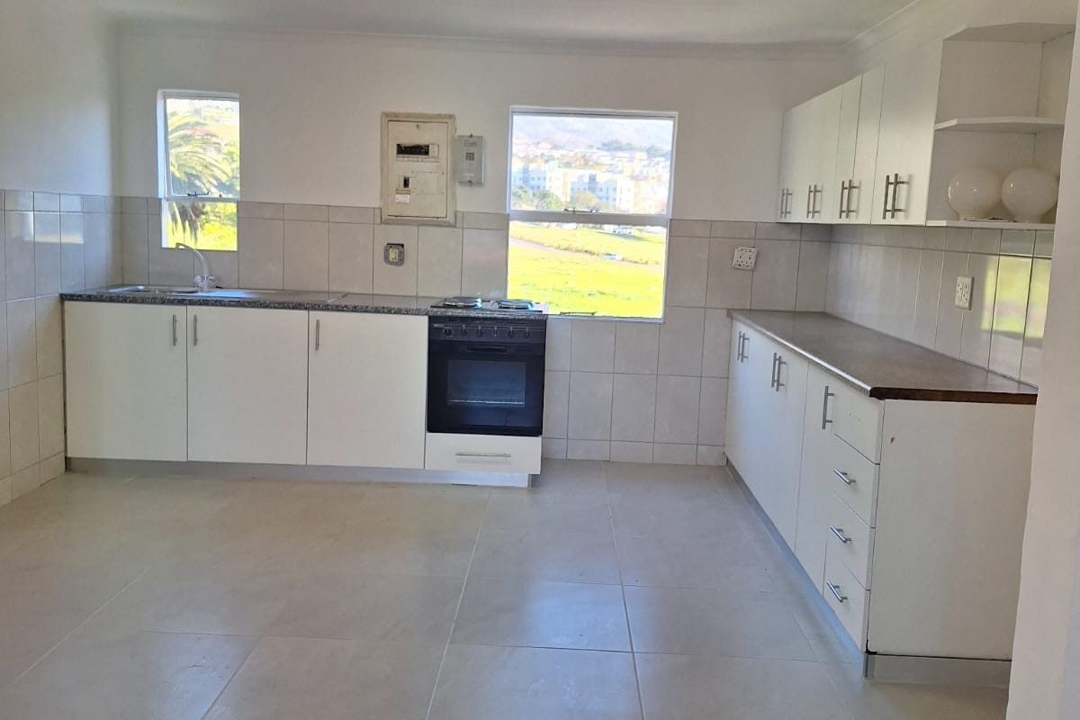 A functional kitchen featuring white cabinetry, tiled flooring, tiled splashbacks, and a built-in stove, offering a clean and practical workspace.