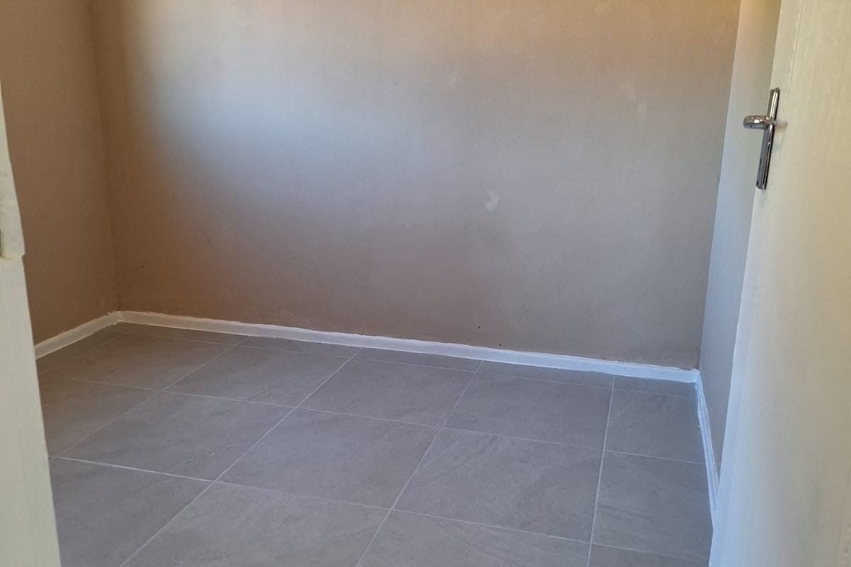 An empty bedroom featuring neutral-toned walls and modern grey floor tiles, providing a clean and versatile space ready for personalization.