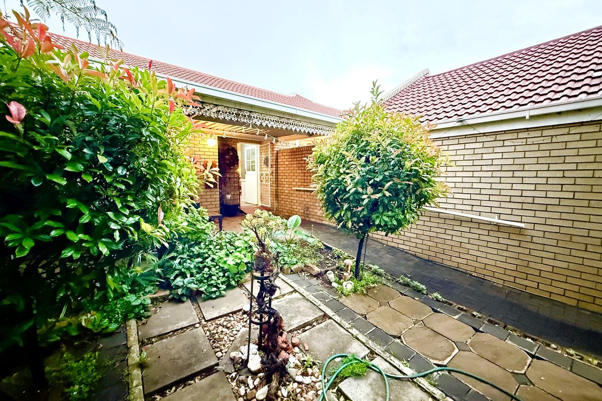A private courtyard garden featuring paved walkways, established shrubbery, and a covered patio area leading to the main entrance.