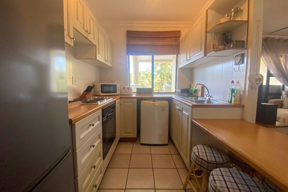 A functional galley-style kitchen featuring white cabinetry, laminate countertops, tiled flooring, and a built-in oven with a cooktop.