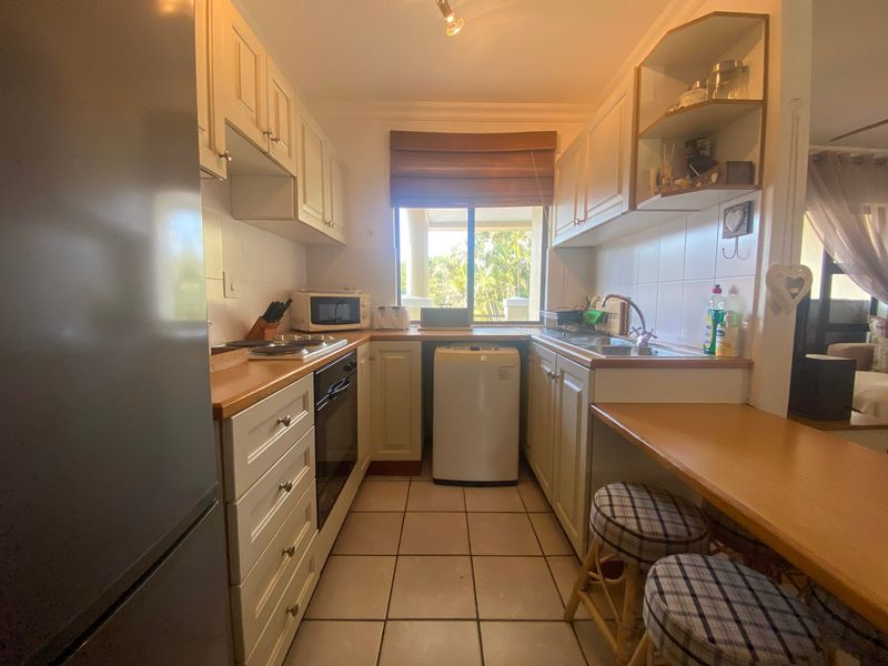 A functional galley-style kitchen featuring white cabinetry, laminate countertops, tiled flooring, and a built-in oven with a cooktop.