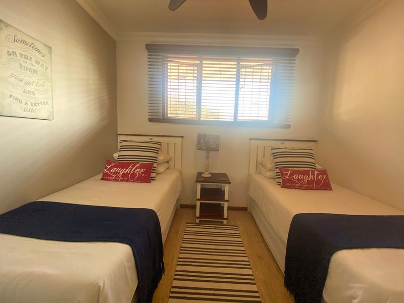 A functional bedroom featuring laminate flooring, wooden blinds, and a ceiling fan, providing a comfortable space for rest.