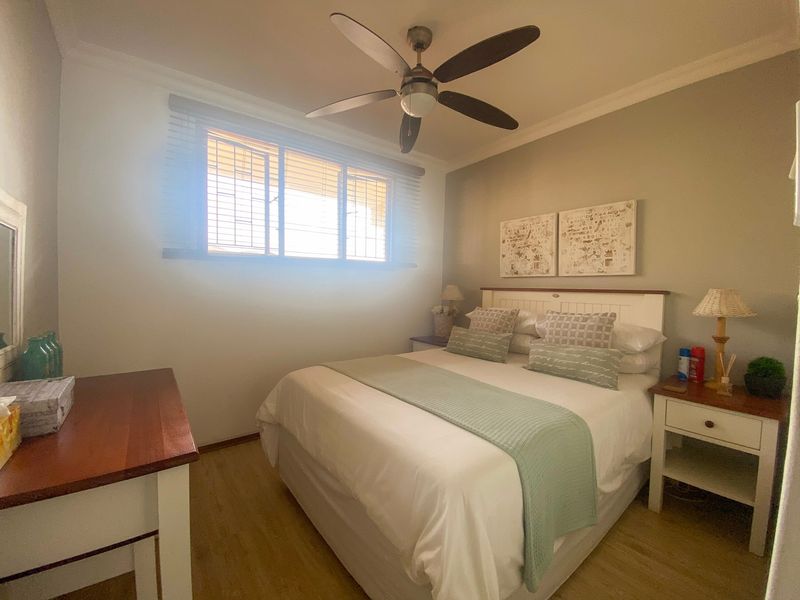 A well-maintained bedroom featuring laminate flooring, a ceiling fan, and window blinds, offering a comfortable and functional living space.