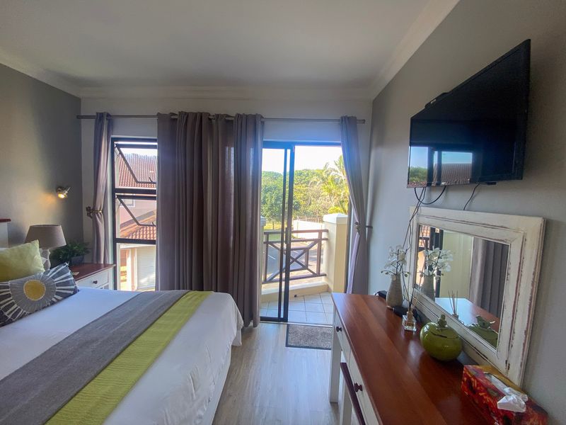 A well-maintained bedroom featuring laminate flooring, wall-mounted television, and direct access to a private balcony through sliding glass doors.
