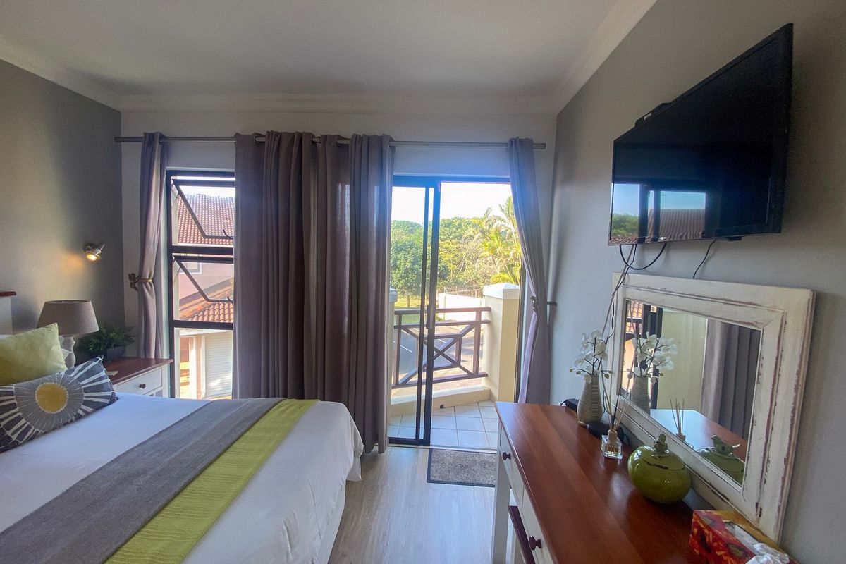 A well-maintained bedroom featuring laminate flooring, wall-mounted television, and direct access to a private balcony through sliding glass doors.