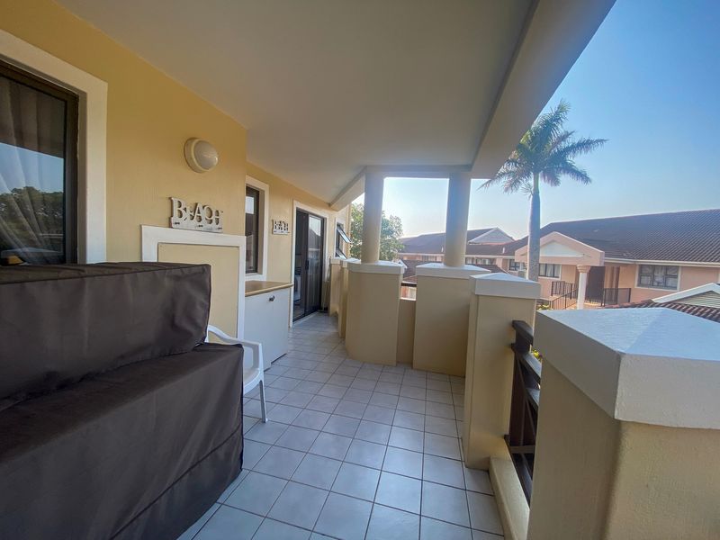 A spacious covered balcony featuring tiled flooring, built-in cabinetry, and a balustrade, offering an open outdoor area suitable for relaxation.