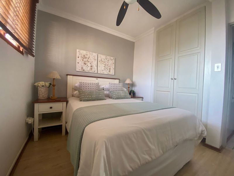 A well-maintained bedroom featuring laminate flooring, a ceiling fan, and built-in wardrobe storage with classic panel detailing.