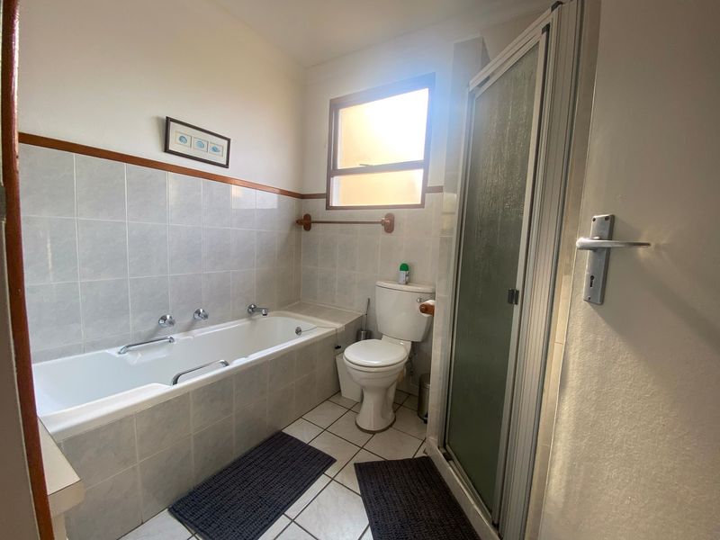 A functional bathroom featuring a built-in bathtub, separate shower enclosure, and toilet with neutral wall and floor tiling.