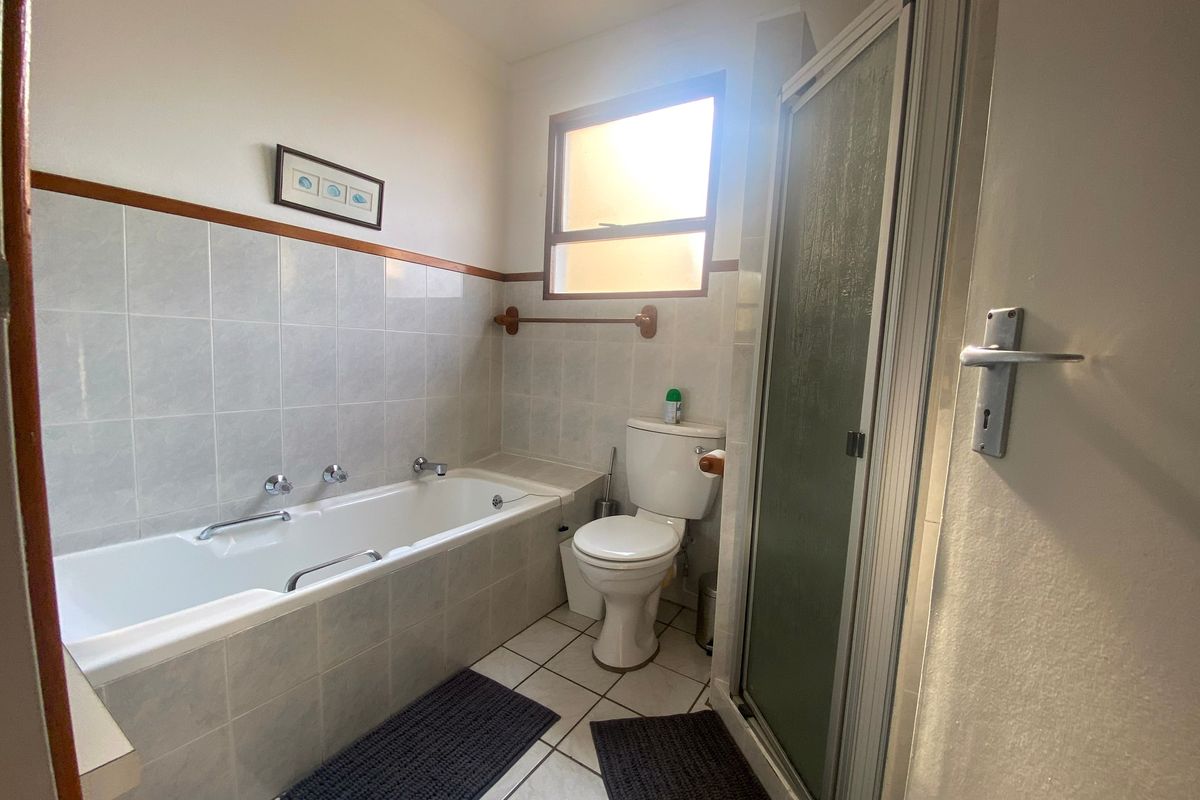 A functional bathroom featuring a built-in bathtub, separate shower enclosure, and toilet with neutral wall and floor tiling.