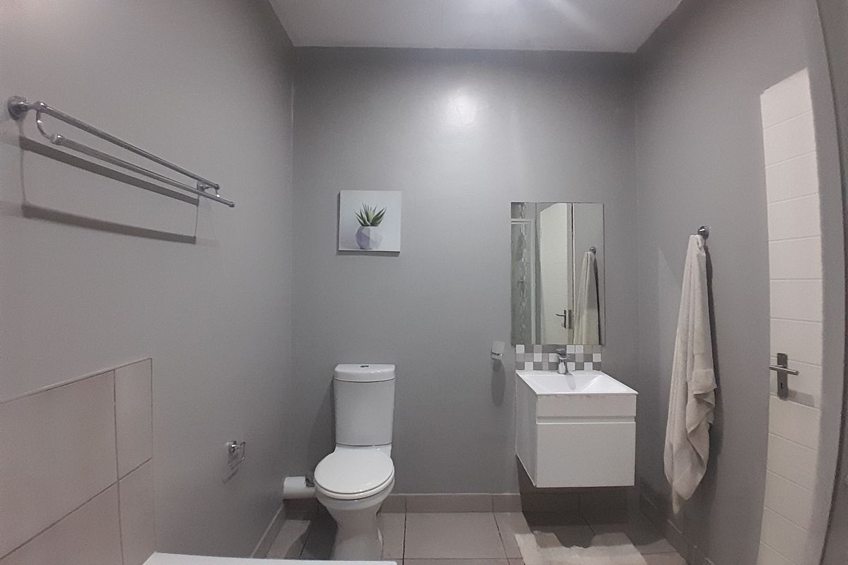 A functional bathroom featuring a wall-mounted vanity, ceramic toilet, and neutral grey wall finishes with tiled flooring.