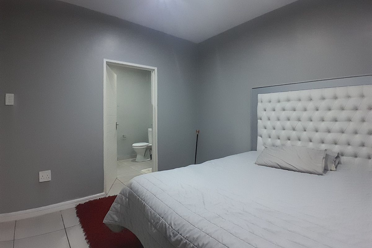 A well-maintained bedroom featuring neutral grey walls, tiled flooring, and direct access to an en-suite bathroom.