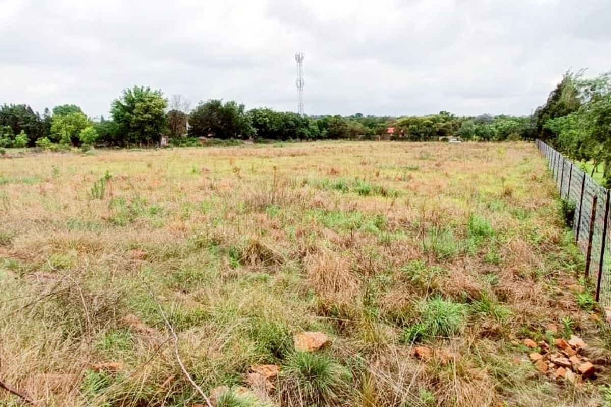 A large, undeveloped plot of land featuring natural grass cover and perimeter wire mesh fencing.