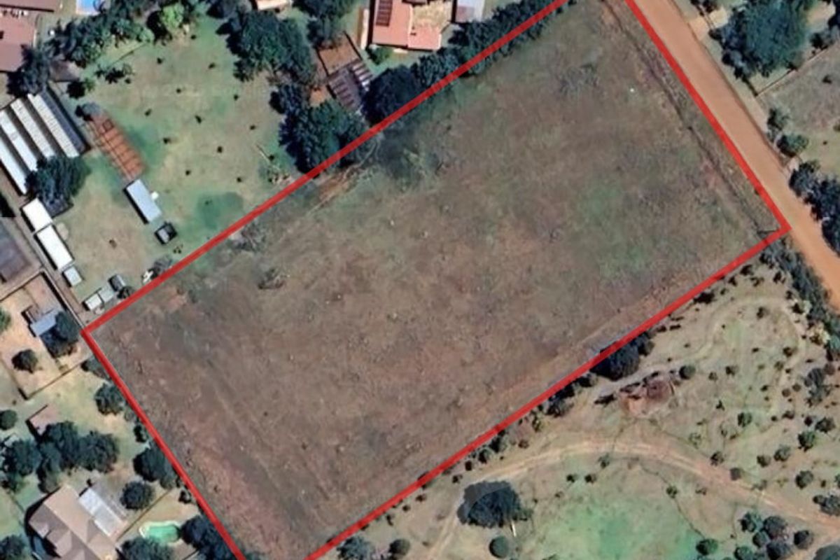 Aerial view of a large, vacant rectangular plot of land with a red boundary outline, situated in a semi-rural residential area.