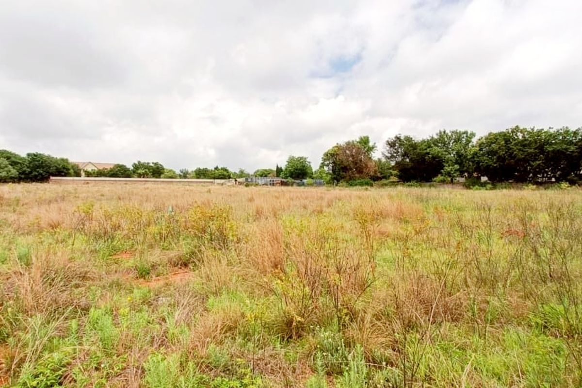 A wide, undeveloped plot of land featuring natural grass, mature trees, and perimeter wire fencing.