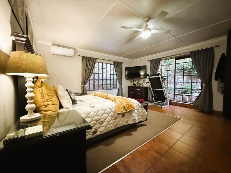 Spacious bedroom featuring tiled flooring, a ceiling fan, and a wall-mounted air conditioning unit with large windows providing natural light.