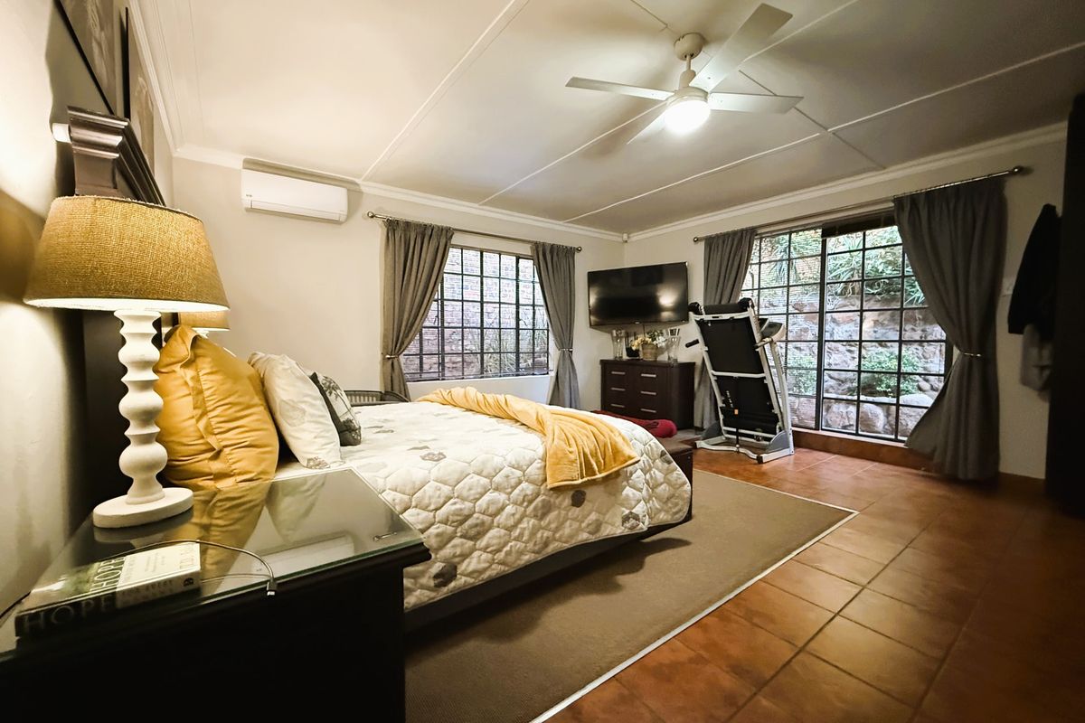 Spacious bedroom featuring tiled flooring, a ceiling fan, and a wall-mounted air conditioning unit with large windows providing natural light.