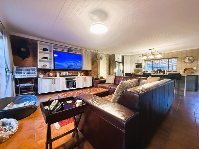 Spacious open-plan living area featuring a built-in media unit, exposed brick feature wall, and a modern kitchen with a central island and breakfast bar.