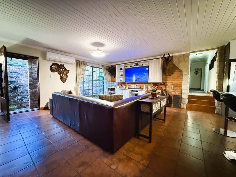 Spacious living room featuring tiled flooring, a timber-paneled ceiling, built-in media cabinetry, and an exposed brick feature wall with direct outdoor access.