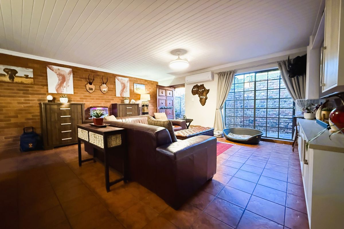 Spacious living area featuring exposed brick walls, timber panelled ceiling, tiled flooring, and a split system air conditioner with access to an outdoor area.