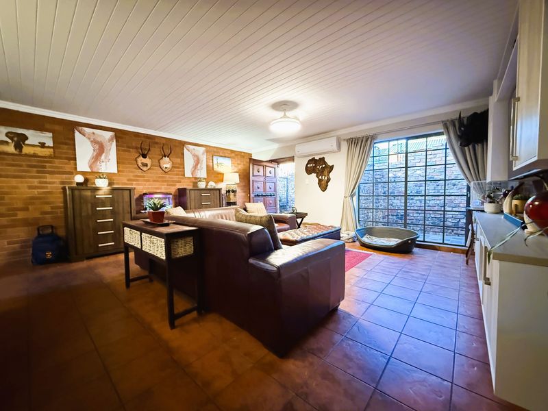 Spacious living area featuring exposed brick walls, timber panelled ceiling, tiled flooring, and a split system air conditioner with access to an outdoor area.