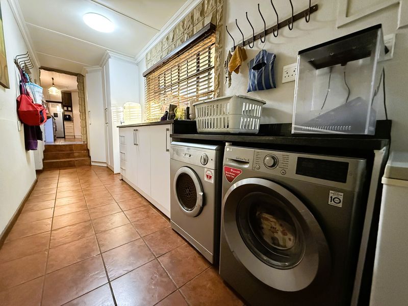 Functional laundry room featuring tiled flooring, built-in cabinetry with stone countertops, and a stone feature wall, providing practical utility space.